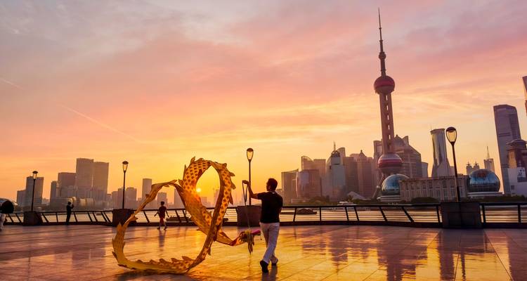 Iemand die lint dansen beoefent op de Bund bij zonsopgang met de gloeiende skyline van Shanghai op de achtergrond.