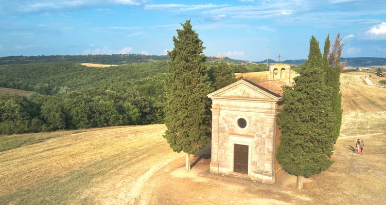 Pequeña capilla de piedra rodeada de cipreses en el campo toscano bañado por el sol.