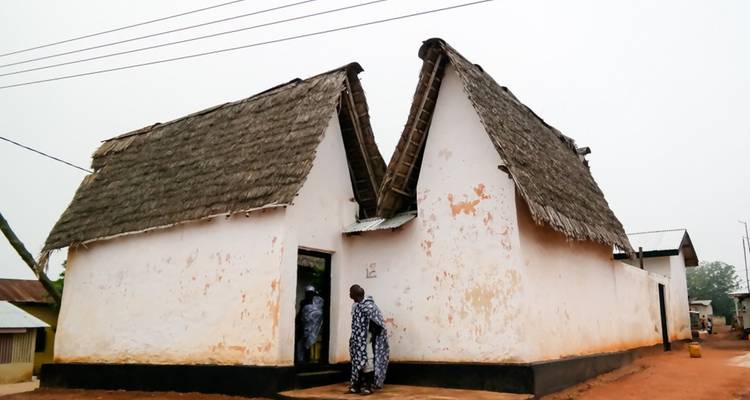 Bâtiment blanc en adobe simple avec des toits de chaume jumeaux dans un village ghanéen.