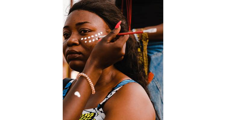 Portrait rapproché d'une femme se faisant appliquer du maquillage facial à pois blancs lors d'une célébration culturelle.