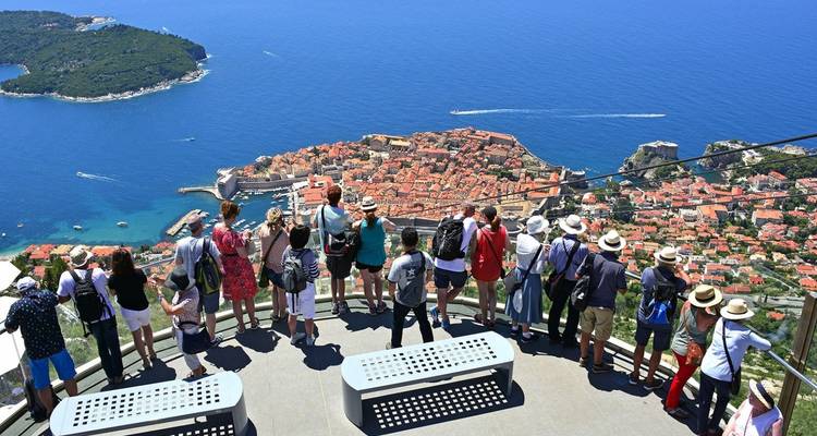 Large group of tourists at a high viewpoint looking down over the red-roofed old town and blue Adriatic Sea