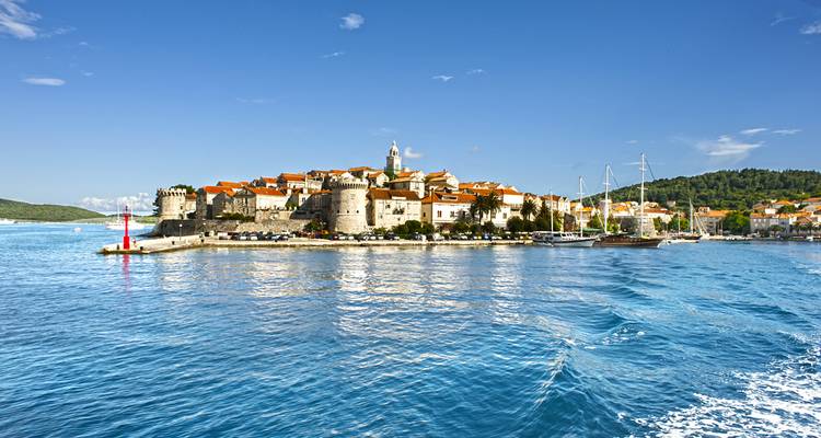 Fortified medieval island town of Korčula viewed from the water with boats and blue sea in foreground