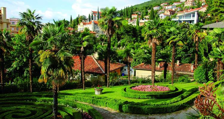 Lush terraced garden with palms and manicured hedges overlooking hillside villas in a coastal resort town