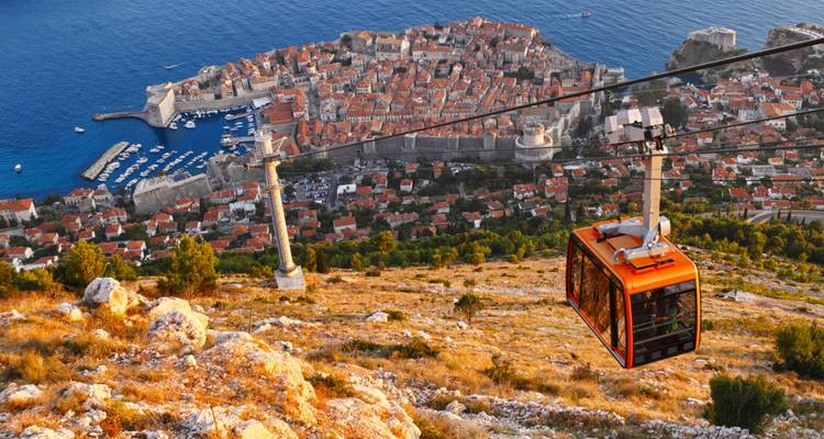 A bright orange cable car ascends above the terracotta-roofed old town of Dubrovnik with the deep blue Adriatic Sea in the background.