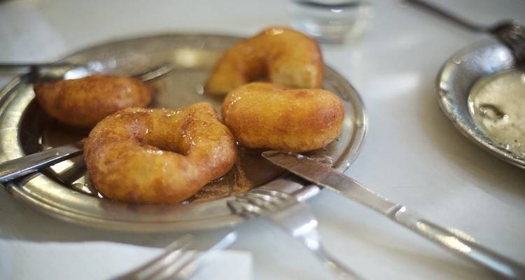 Une assiette de beignets grecs glacés au miel est posée dans un plat en métal, entouré de fourchettes et de couteaux.