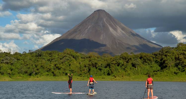 Stand-up paddleboarders glijden over een meer naar de imposante kegel van de vulkaan Arenal.