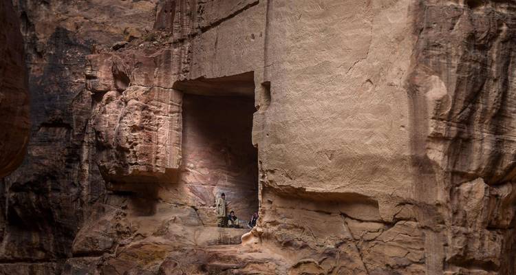 Les visiteurs se tiennent éclipsés sous les imposants murs de grès sculptés à l'intérieur de l'architecture rupestre de Petra.