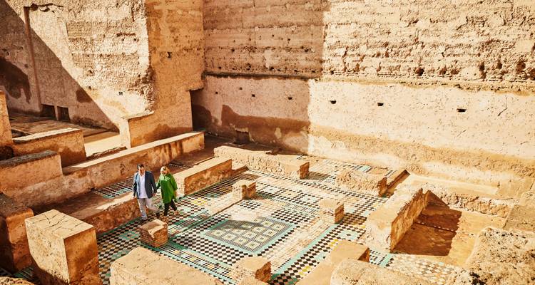Deux visiteurs explorent des ruines ensoleillées aux sols en mosaïque à motifs et aux murs en adobe
