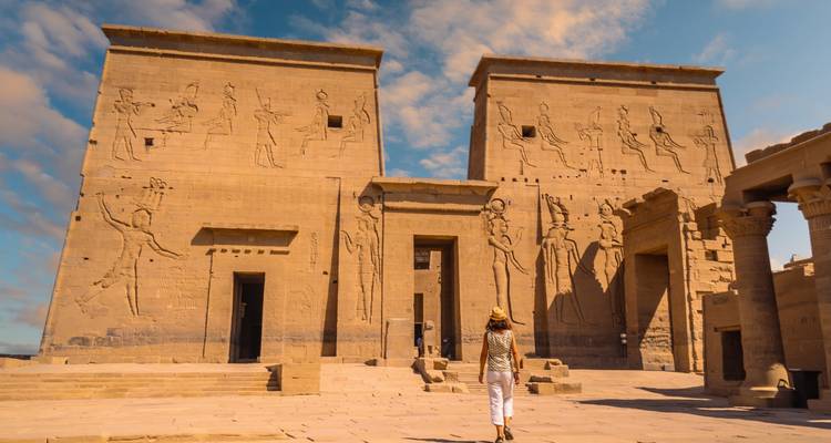 Besucher im Sonnenhut geht auf Sandsteintempelmauern zu, die mit Reliefs geschmückt sind