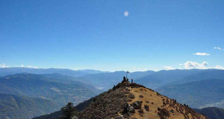 Dos excursionistas de pie en una estrecha cresta con vistas panorámicas del Himalaya extendiéndose hacia el horizonte.