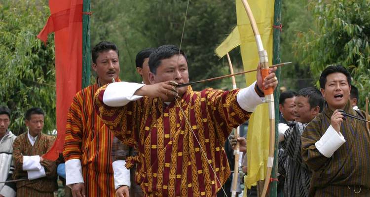 Un arquero butanés con atuendo tradicional tira de su arco durante una animada competencia de tiro con arco en el pueblo.