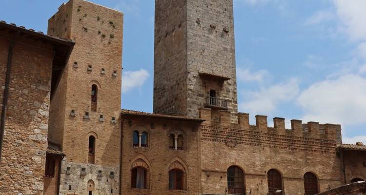 Las altas torres de piedra medieval se alzan sobre los tejados de San Gimignano bajo un cielo azul.