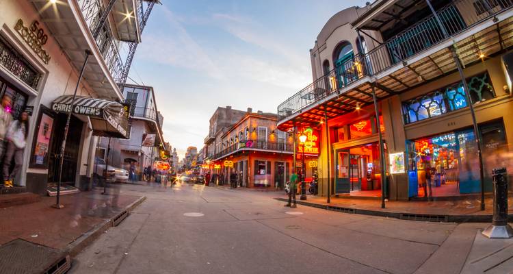 Neon-beleuchtete Bourbon Street bei Einbruch der Dunkelheit mit Besuchern, die zwischen historischen Balkonen spazieren