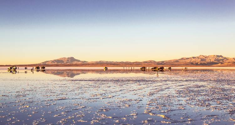 Les jeeps de la visite touristique se reflètent dans l'eau lisse comme un miroir du Salar de Uyuni au coucher du soleil