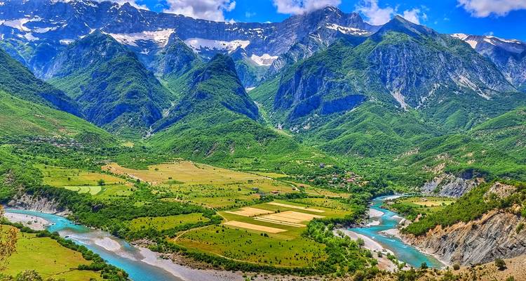 Une vue aérienne vivante d'une rivière turquoise sinueuse traversant de luxuriantes vallées verdoyantes sous d'imposants sommets couverts de neige.
