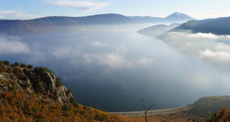 A hazy panoramic view over a mist-filled lake and surrounding autumnal hills from a high lookout.