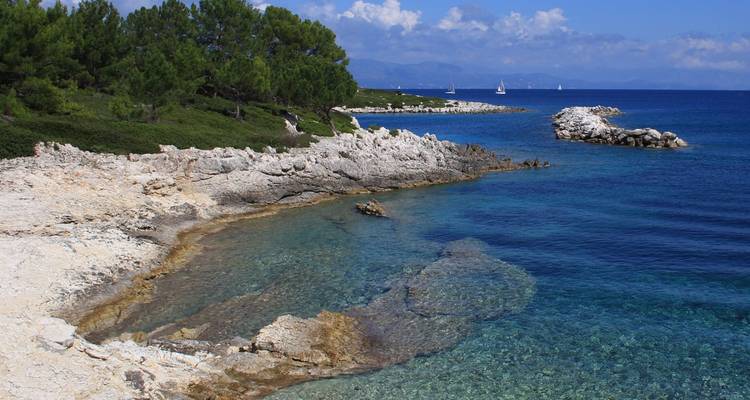 Felsige weiße Kalksteinküste trifft auf unglaublich klares saphirblaues Wasser unter einem sonnigen Himmel.
