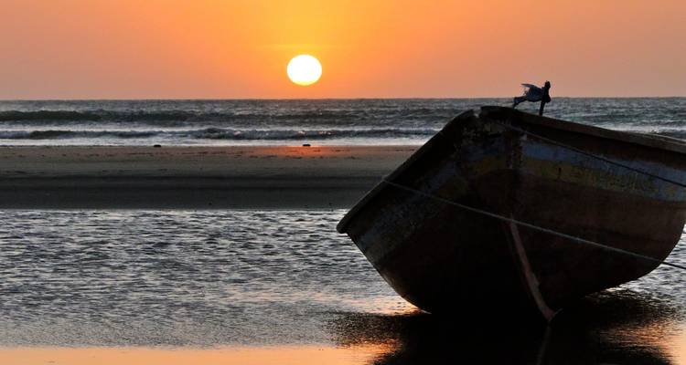 Bateau en bois échoué en silhouette contre un coucher de soleil océanique orange sur la côte nord du Brésil
