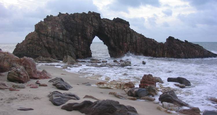 L'arche rocheuse Pedra Furada s'élevant de l'écume de l'Atlantique sous un ciel nuageux