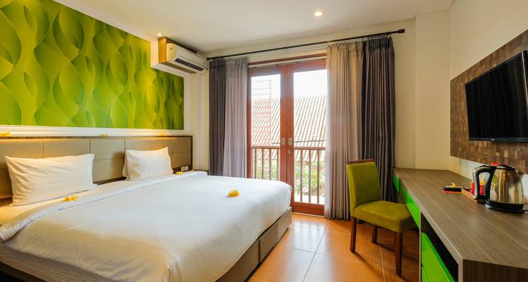 Lichte hotelkamer met kingsize bed, groene accentmuur en balkondeur met uitzicht op pannendaken.