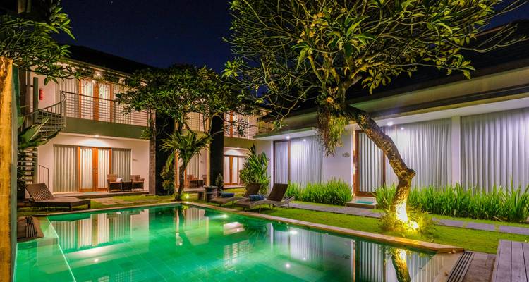 Sereen nachtbeeld van een boutique villa met verlichte zwembad omringd door tropische planten en ligstoelen.