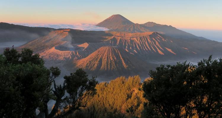 La luz del amanecer golpeando las crestas del Monte Bromo y la caldera circundante con nubes abajo.