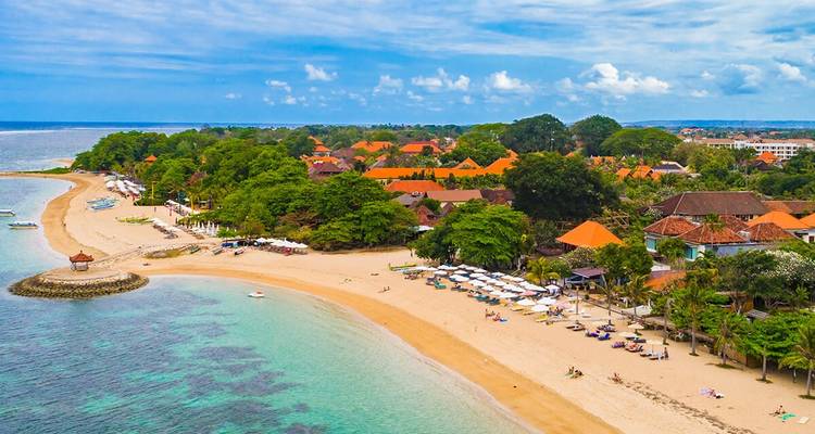 Vista aérea de la playa de Sanur con agua turquesa, arena amarilla y filas de sombrillas.