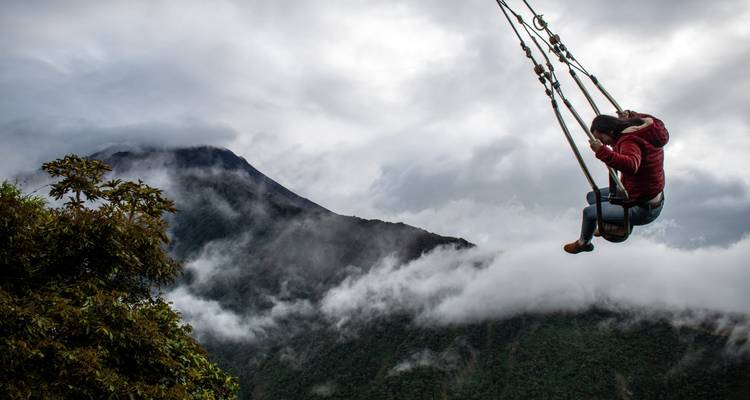 Abenteurer schwingt sich über ein wolkenerfülltes Tal, wobei sich ein nebeliger Vulkangipfel im Hintergrund erhebt.
