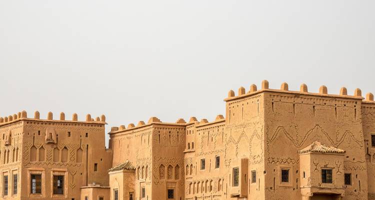 Bâtiments de casbah en adobe aux toits crénelés se dressant contre un ciel désertique pâle.