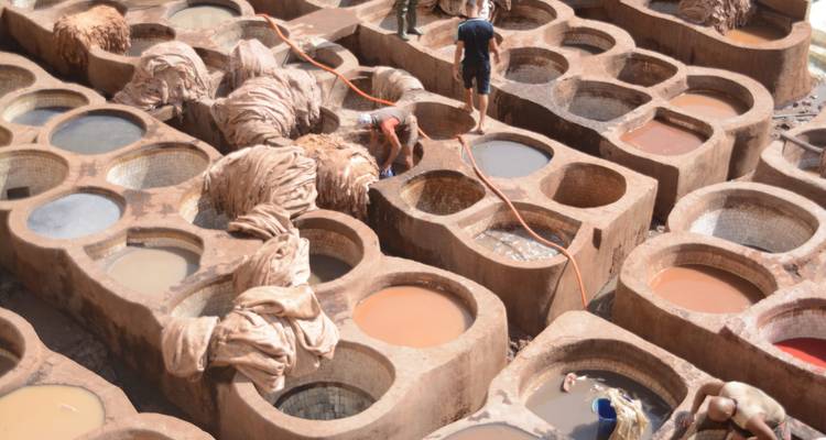Les ouvriers manipulent les peaux d'animaux dans les cuves en pierre circulaires d'une tannerie traditionnelle remplies de liquides colorés.