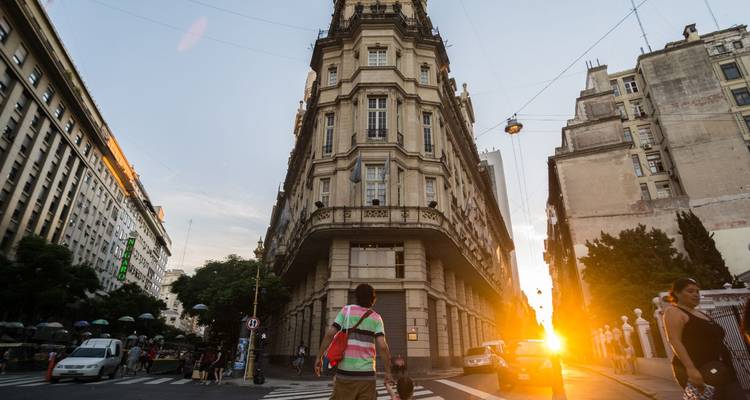 Historische Straße in der Innenstadt von Buenos Aires mit verziertem Eckgebäude, das im goldenen Licht des Sonnenuntergangs erstrahlt.