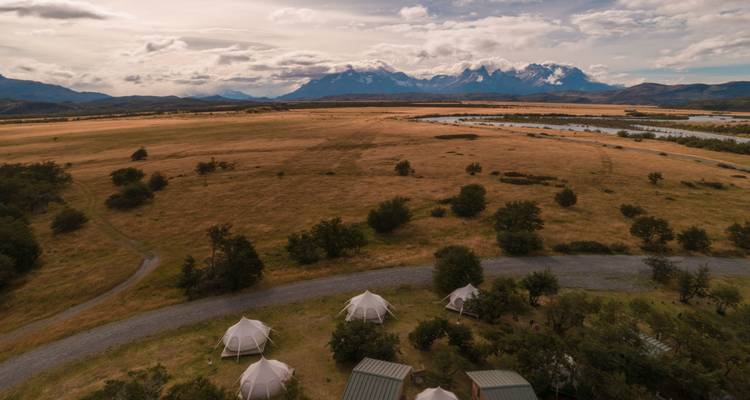 Luftaufnahme von Glamping-Zelten auf goldenen Ebenen mit dem dramatischen Massiv der Torres del Paine im Hintergrund