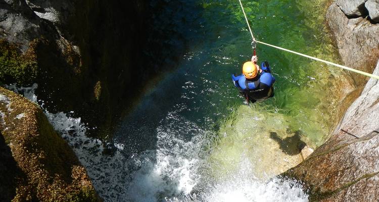 Aventurier en combinaison de plongée et casque suspendu par une corde au-dessus d'une piscine de canyon d'un vert émeraude cristallin et d'une cascade à Peneda-Geres