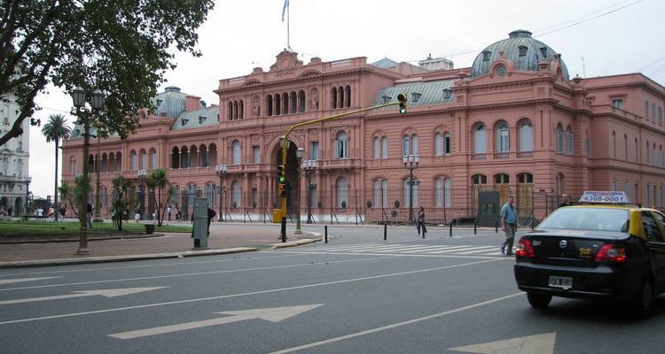 Het roze getinte Casa Rosada staat indrukwekkend langs een straat in Buenos Aires terwijl een zwart-gele taxi voorbijrijdt.