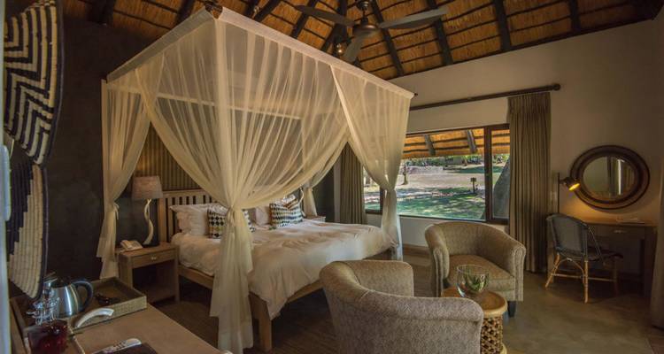Chambre de lodge safari rustique avec lit à baldaquin et toit en chaume