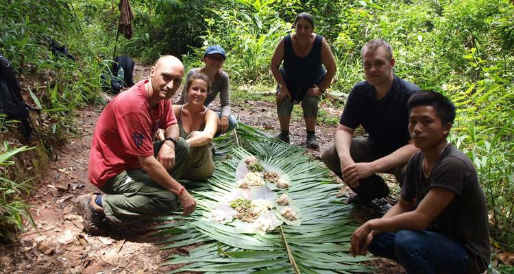 Pequeño grupo de trekking sentado alrededor de una comida improvisada con hojas en el medio de la selva