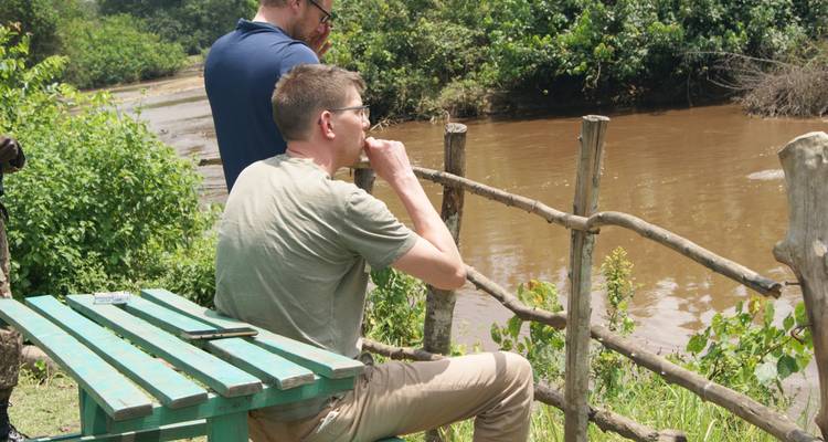 Los viajeros jóvenes descansan en un mirador rústico a orillas del río, observando el agua lodosa y el bosque.