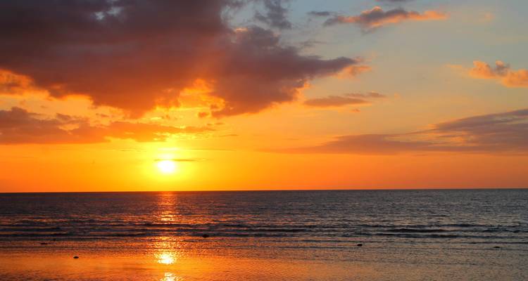 Un soleil orange éclatant se couchant sur des eaux océaniques calmes avec des ondulations douces et un ciel lumineux.