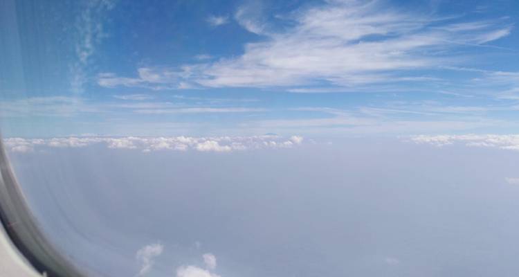 Vue depuis le hublot d'un avion montrant des nuages lointains et un horizon brumeux sur fond de ciel bleu.
