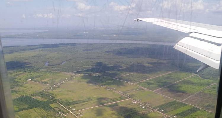 Vue à travers un hublot d'avion rayé de terres agricoles en patchwork, de rivière et de l'aile de l'aéronef.