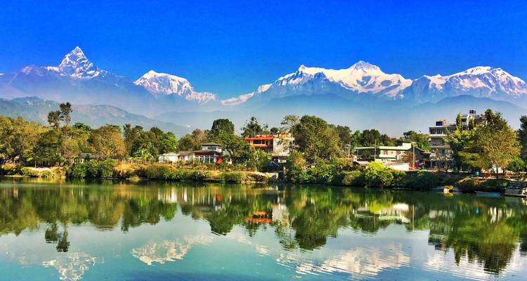 Calm lake reflects Pokhara’s low skyline beneath crisp white Himalayan peaks.