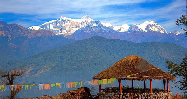 Open shelter with fluttering prayer flags overlooks distant snowy summits.