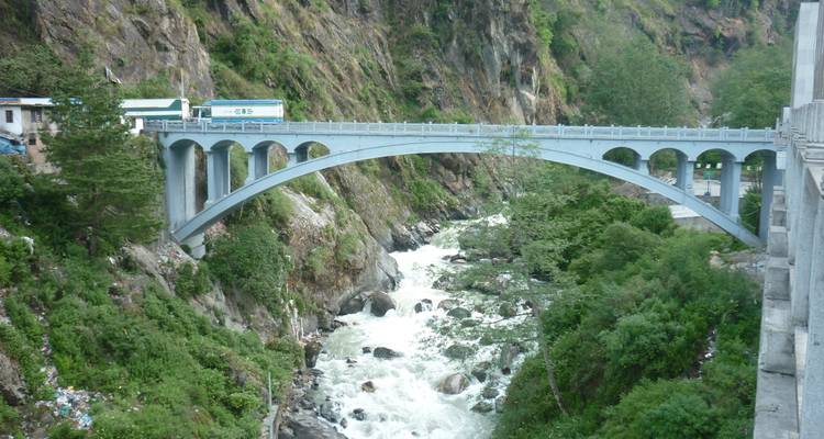 Concrete arch bridge carries a road high over a fast-flowing mountain river in a deep gorge.