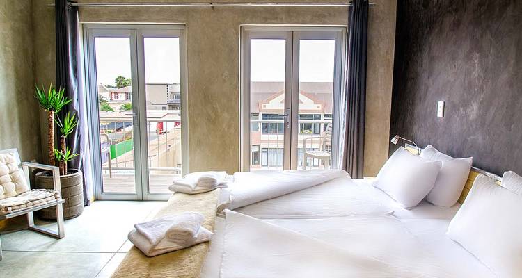 Chambre d'hôtel minimaliste moderne avec une literie d'un blanc immaculé et des portes-fenêtres donnant sur les toits de la ville.