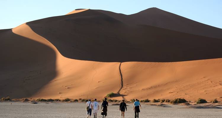 Trekking en petit groupe à travers des dunes de sable orange imposantes projetant de longues ombres dans la douce lumière du matin.