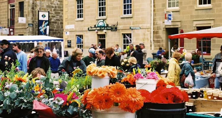 Belebter Außenmarkt mit leuchtenden Blumenständen und Menschenmengen auf einem historischen Marktplatz in einer tasmanischen Stadt.