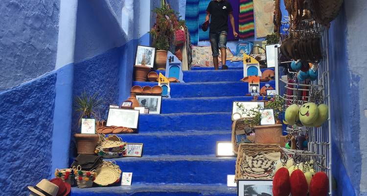 Escalier bleu à Chefchaouen bordé d'objets artisanaux colorés tandis qu'un visiteur monte vers le haut.
