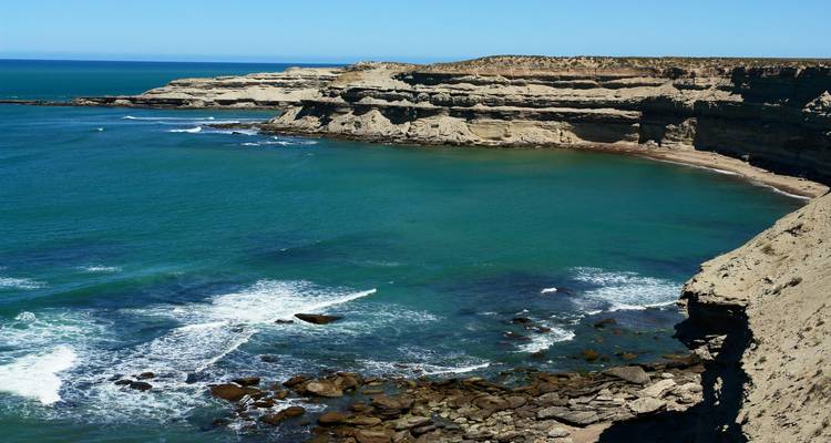 Baie turquoise encadrée par des falaises de grès escarpées et des vagues déferlantes