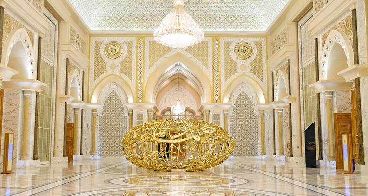 Suntuoso salón de mármol del Qasr Al Watan con una escultura dorada en el centro y una araña de cristal.