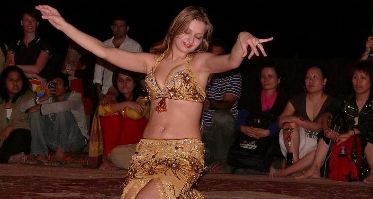 Una bailarina del vientre actúa con un traje brillante para una audiencia sentada en alfombras en un campamento del desierto.